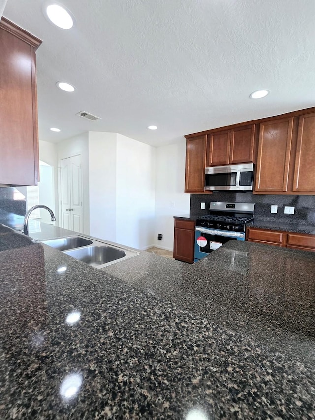 kitchen with a textured ceiling, stainless steel appliances, dark stone countertops, and sink