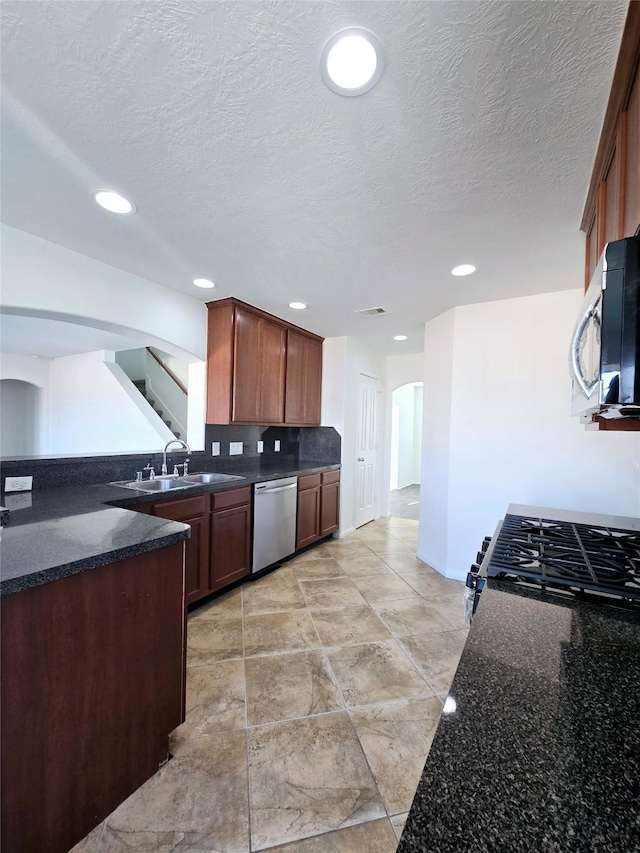 kitchen with a textured ceiling, dark stone countertops, sink, and appliances with stainless steel finishes