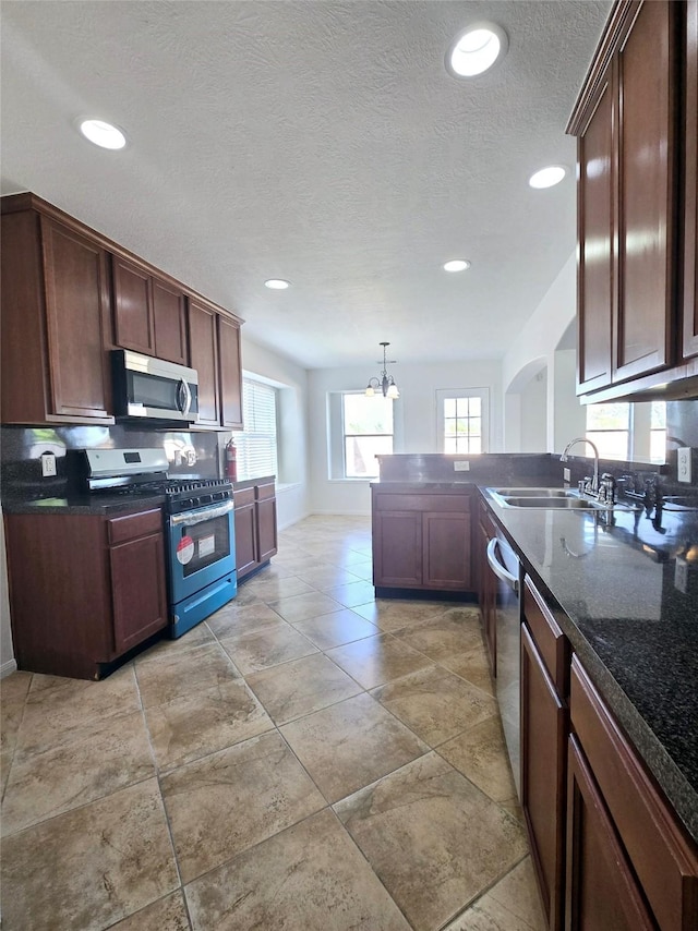 kitchen with a textured ceiling, stainless steel appliances, sink, pendant lighting, and a notable chandelier