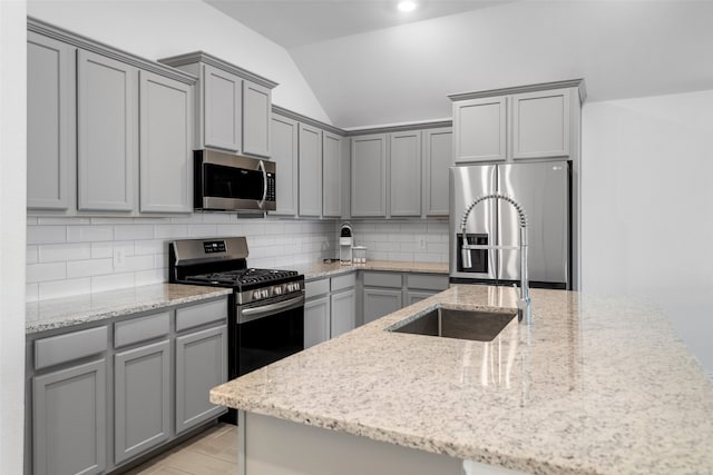 kitchen with lofted ceiling, sink, decorative backsplash, light stone countertops, and appliances with stainless steel finishes