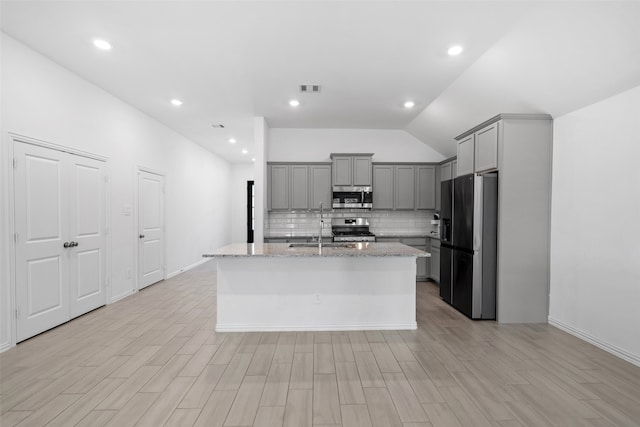 kitchen featuring gray cabinets, light stone countertops, stainless steel appliances, and an island with sink