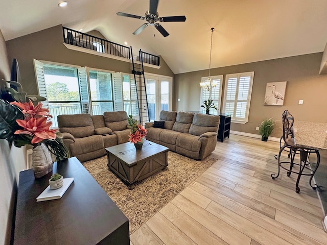 living room with high vaulted ceiling, ceiling fan with notable chandelier, and light wood-type flooring