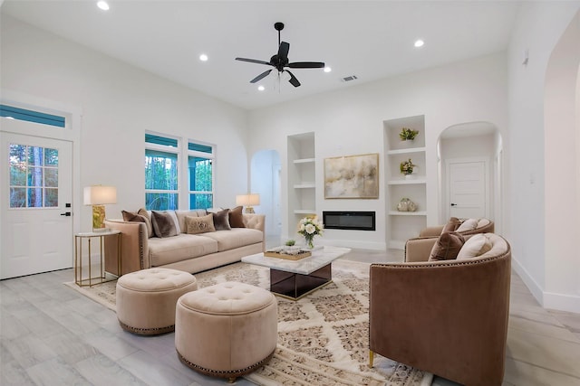 living room with ceiling fan, built in shelves, and light hardwood / wood-style flooring