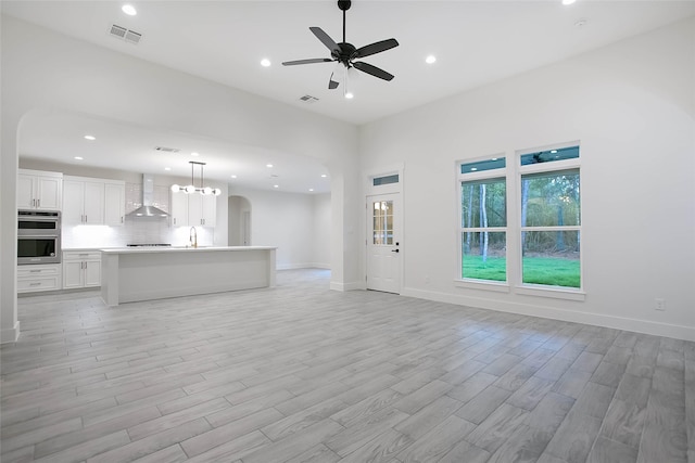 unfurnished living room with ceiling fan, sink, and light wood-type flooring