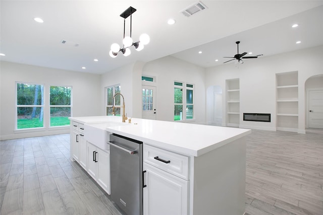 kitchen featuring ceiling fan with notable chandelier, white cabinets, built in shelves, hanging light fixtures, and a kitchen island with sink