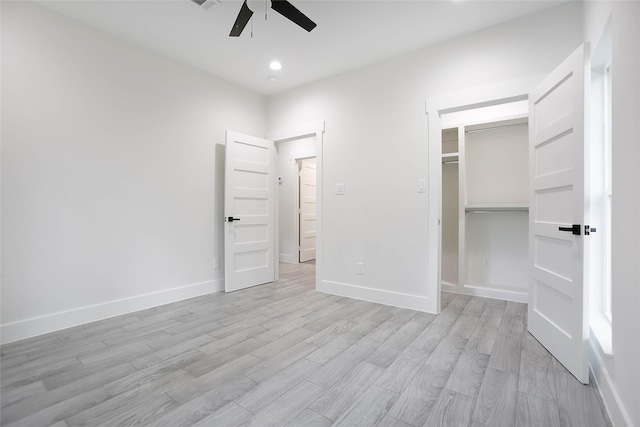 unfurnished bedroom with ceiling fan, a walk in closet, a closet, and light hardwood / wood-style flooring