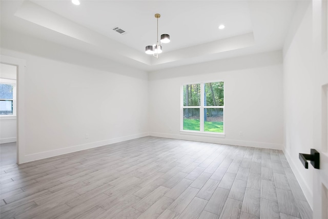 empty room with a raised ceiling and light hardwood / wood-style flooring