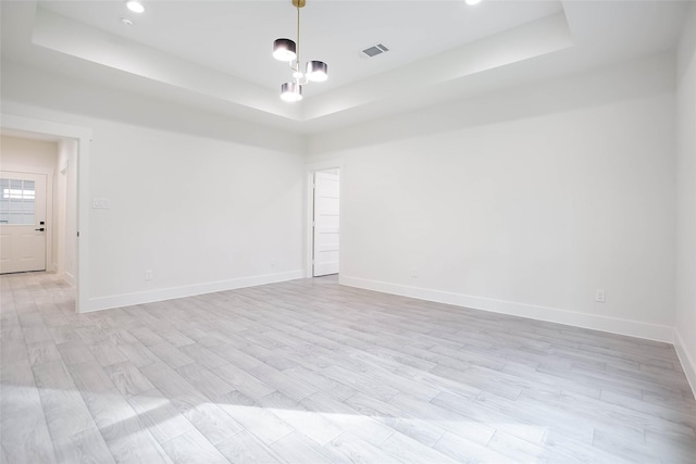 empty room with a tray ceiling and light hardwood / wood-style flooring