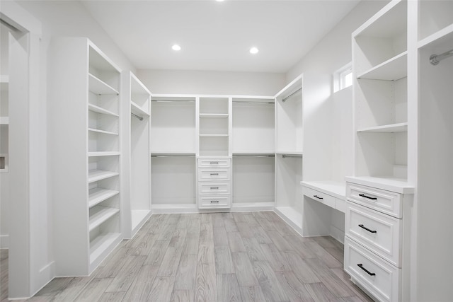 spacious closet with built in desk and light hardwood / wood-style floors