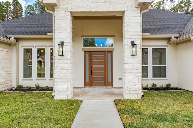 property entrance featuring stucco siding, a lawn, stone siding, and a shingled roof