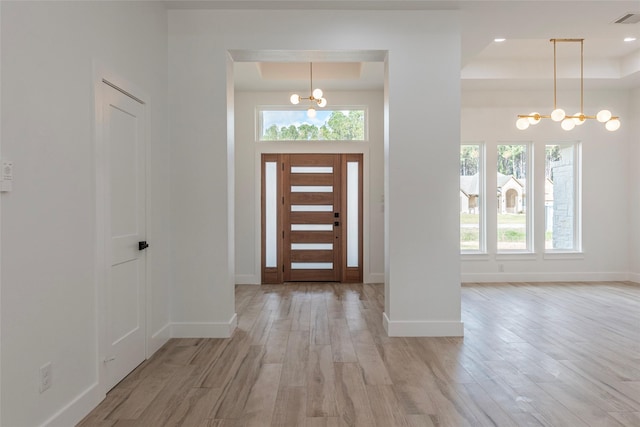 foyer with a notable chandelier, light wood-type flooring, and a tray ceiling