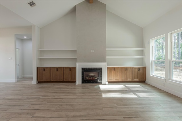 unfurnished living room featuring a tiled fireplace, plenty of natural light, high vaulted ceiling, and light hardwood / wood-style flooring