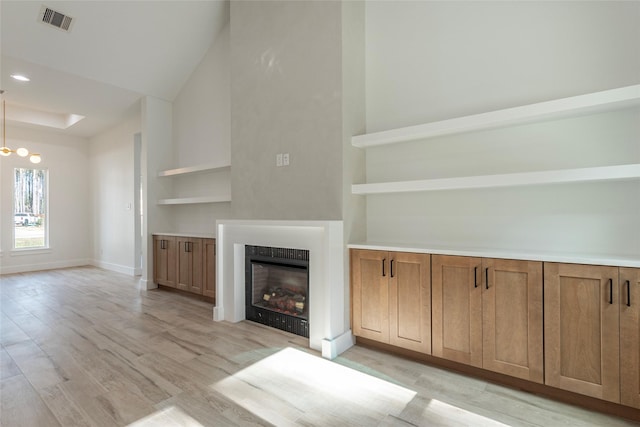 unfurnished living room featuring an inviting chandelier, high vaulted ceiling, and light hardwood / wood-style flooring