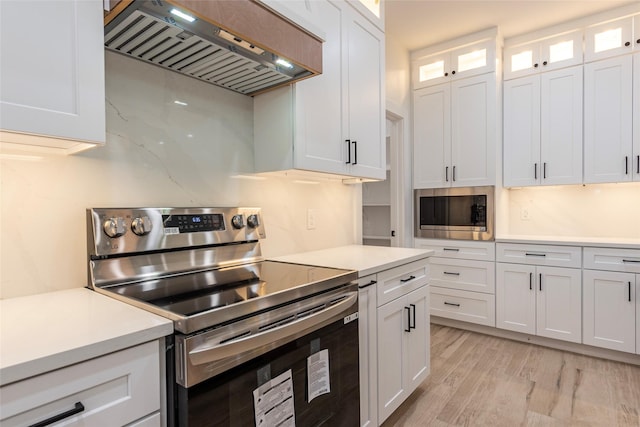 kitchen featuring white cabinets, appliances with stainless steel finishes, light wood-type flooring, and premium range hood