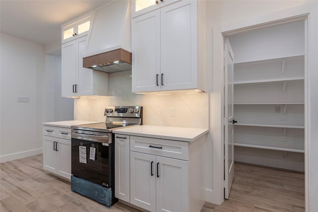 kitchen with white cabinets, premium range hood, light hardwood / wood-style floors, and electric stove