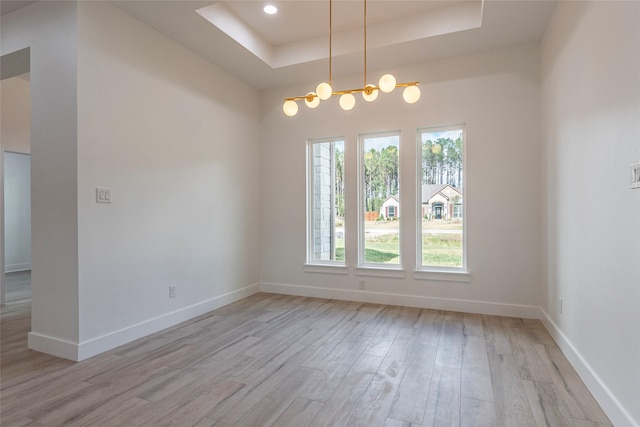 empty room featuring a chandelier, light hardwood / wood-style floors, and a tray ceiling