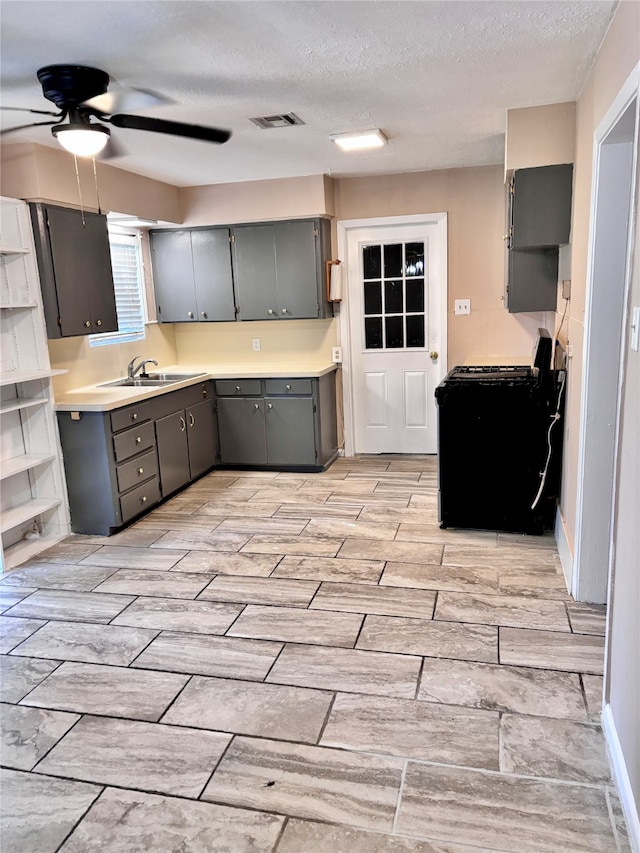 kitchen with gray cabinetry, black range with gas stovetop, a textured ceiling, ceiling fan, and sink