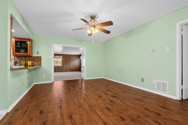 unfurnished living room with sink, hardwood / wood-style flooring, ceiling fan, and wood walls