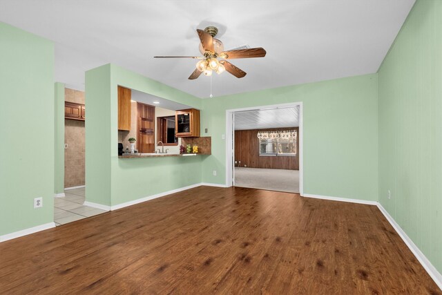 unfurnished living room featuring ceiling fan, wood walls, sink, and light hardwood / wood-style flooring