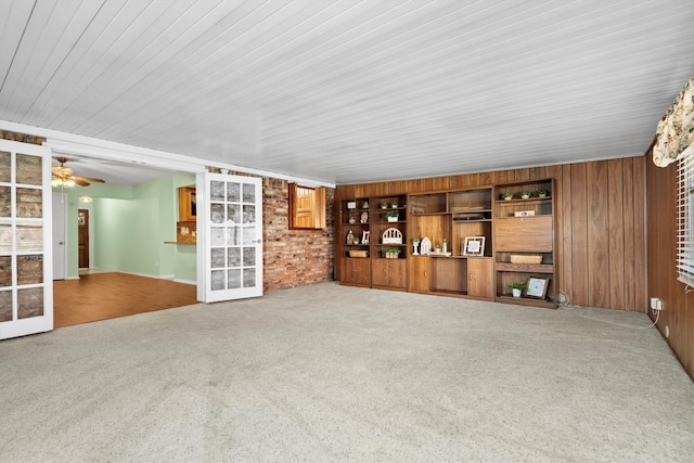 unfurnished living room featuring carpet, ceiling fan, wood walls, and brick wall