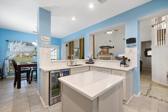 kitchen featuring kitchen peninsula, sink, ceiling fan, white cabinetry, and beverage cooler