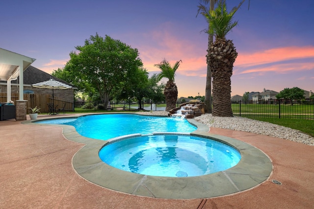 pool at dusk with an in ground hot tub, pool water feature, and a patio area