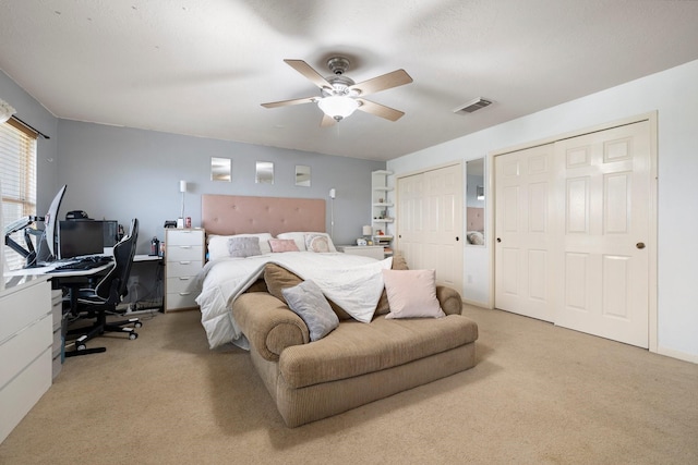 bedroom with ceiling fan, light colored carpet, and multiple closets