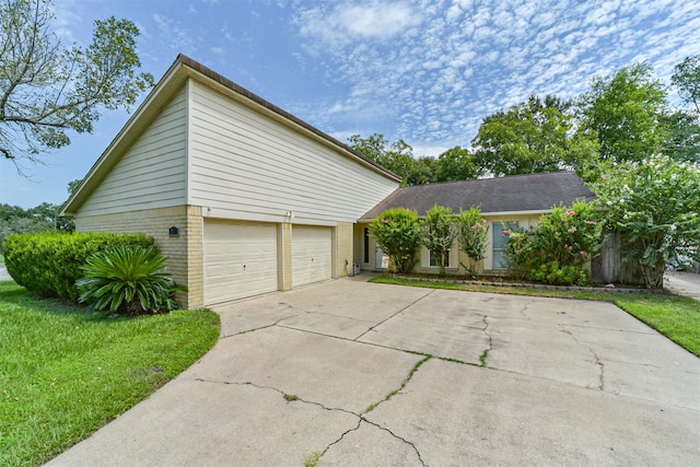 view of side of home with a yard, driveway, brick siding, and an attached garage