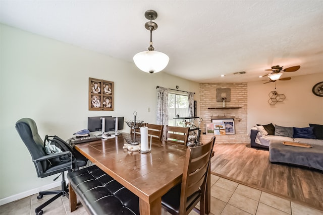 tiled dining space with a ceiling fan, a brick fireplace, visible vents, and baseboards