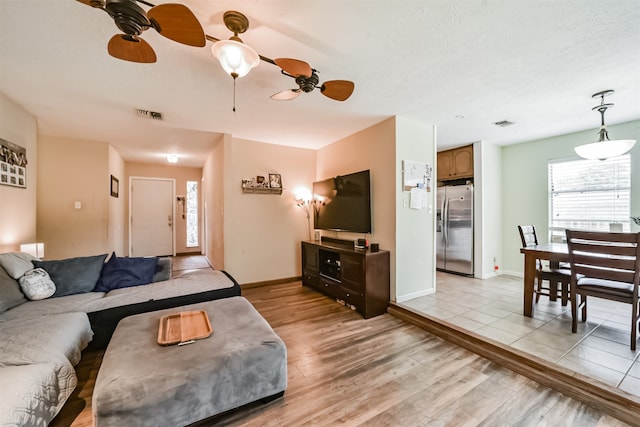 living room featuring ceiling fan, light wood-type flooring, and a textured ceiling