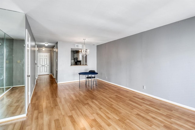 unfurnished room with light wood-type flooring and an inviting chandelier