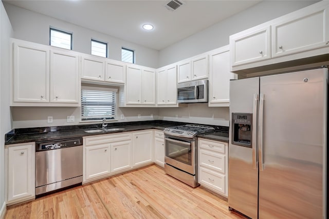 kitchen featuring sink, dark stone countertops, light hardwood / wood-style floors, white cabinets, and appliances with stainless steel finishes