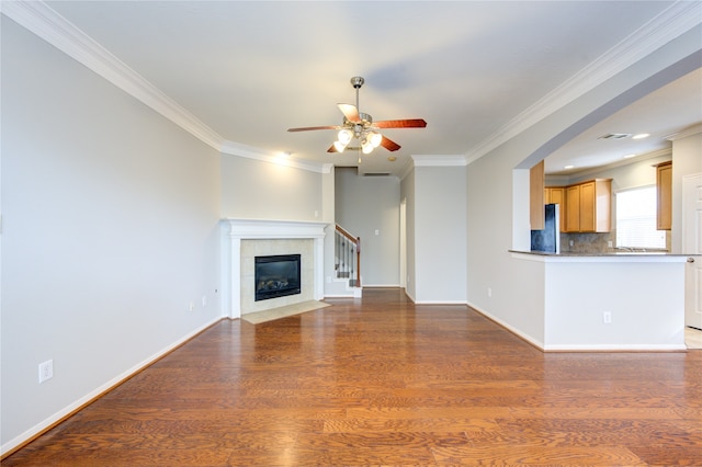 unfurnished living room featuring ceiling fan, dark hardwood / wood-style flooring, ornamental molding, and a tile fireplace