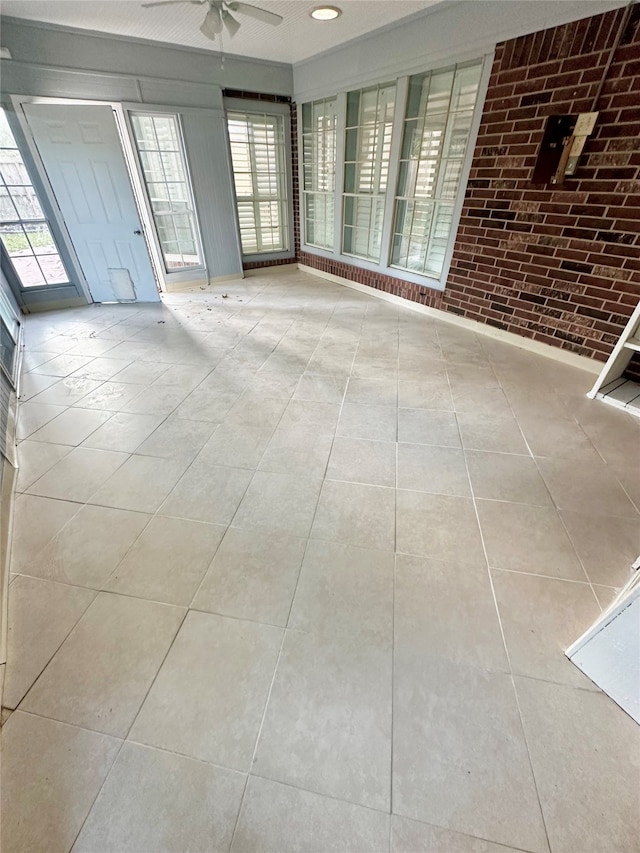 spare room featuring light tile patterned floors, ceiling fan, and brick wall