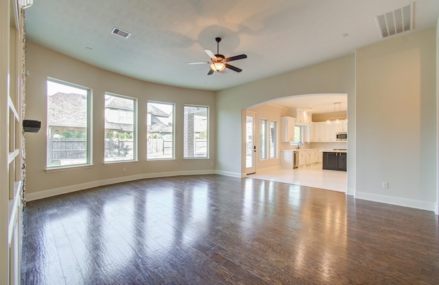 unfurnished living room with ceiling fan, dark wood-type flooring, and a wealth of natural light