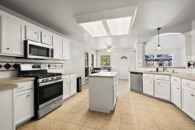 kitchen with decorative backsplash, decorative light fixtures, white cabinetry, stainless steel appliances, and decorative columns