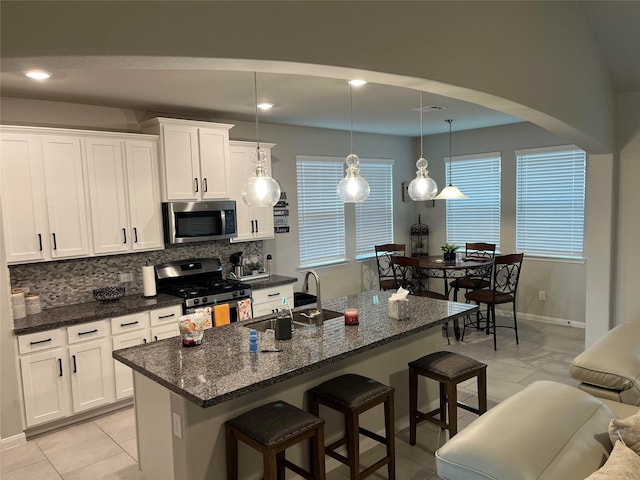 kitchen with appliances with stainless steel finishes, backsplash, a kitchen island with sink, pendant lighting, and white cabinetry