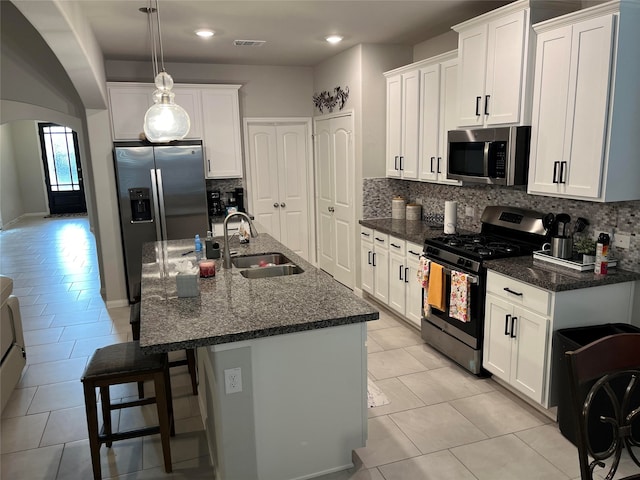 kitchen featuring dark stone counters, stainless steel appliances, sink, white cabinetry, and an island with sink