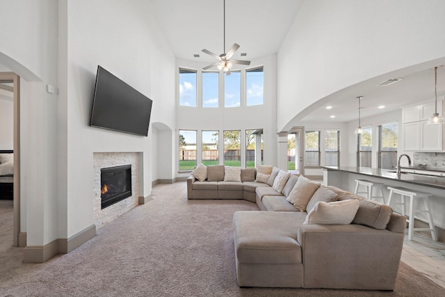 living room featuring ceiling fan, a fireplace, light colored carpet, and a high ceiling