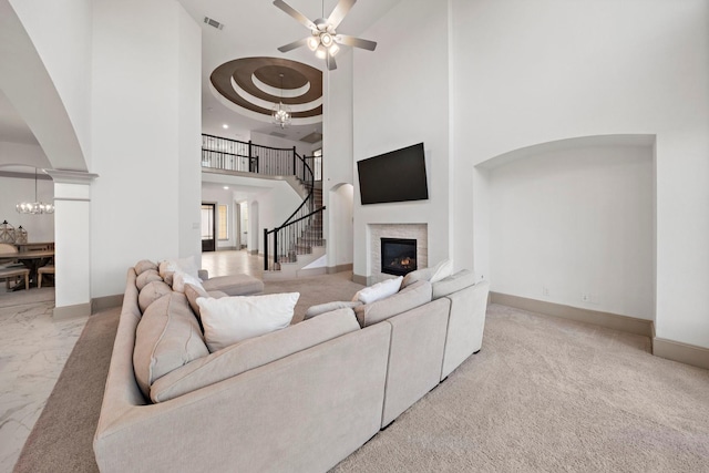 living room with a high ceiling, ceiling fan with notable chandelier, a tray ceiling, and decorative columns