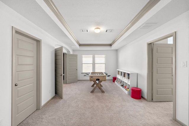 playroom with a textured ceiling, light colored carpet, crown molding, and a tray ceiling