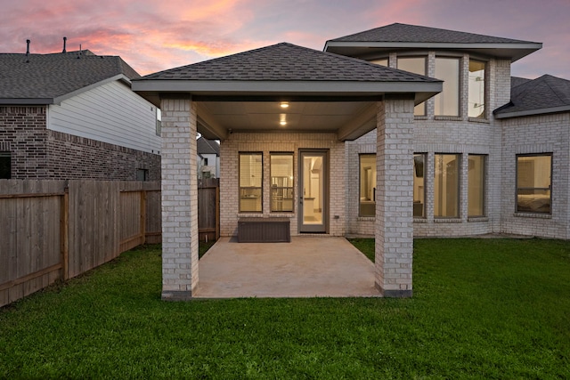 back house at dusk featuring a patio area and a yard