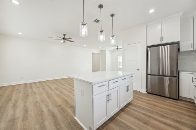 kitchen with white cabinets, stainless steel fridge, a center island, and light stone countertops