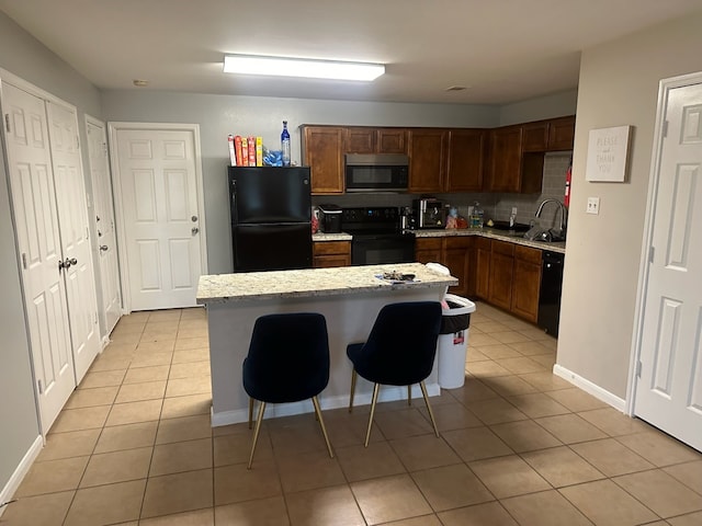 kitchen featuring decorative backsplash, black appliances, a kitchen island, a breakfast bar area, and light tile patterned flooring