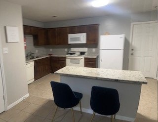 kitchen with a kitchen bar, white appliances, tasteful backsplash, and light tile patterned flooring