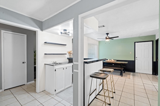 kitchen with white cabinets, a kitchen bar, ceiling fan, and light tile patterned flooring