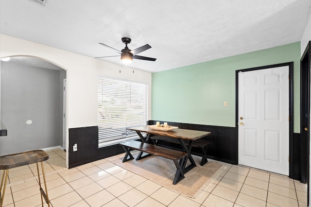 dining area with ceiling fan, wood walls, light tile patterned floors, and a textured ceiling