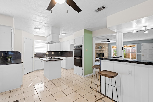 kitchen with black appliances, ceiling fan, a fireplace, white cabinetry, and extractor fan