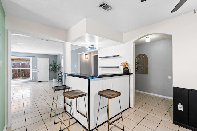 kitchen with a kitchen bar, light tile patterned floors, a textured ceiling, and ceiling fan