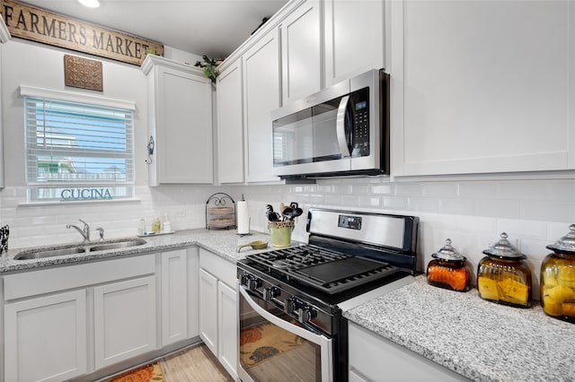 kitchen with white cabinets, sink, decorative backsplash, light stone countertops, and stainless steel appliances